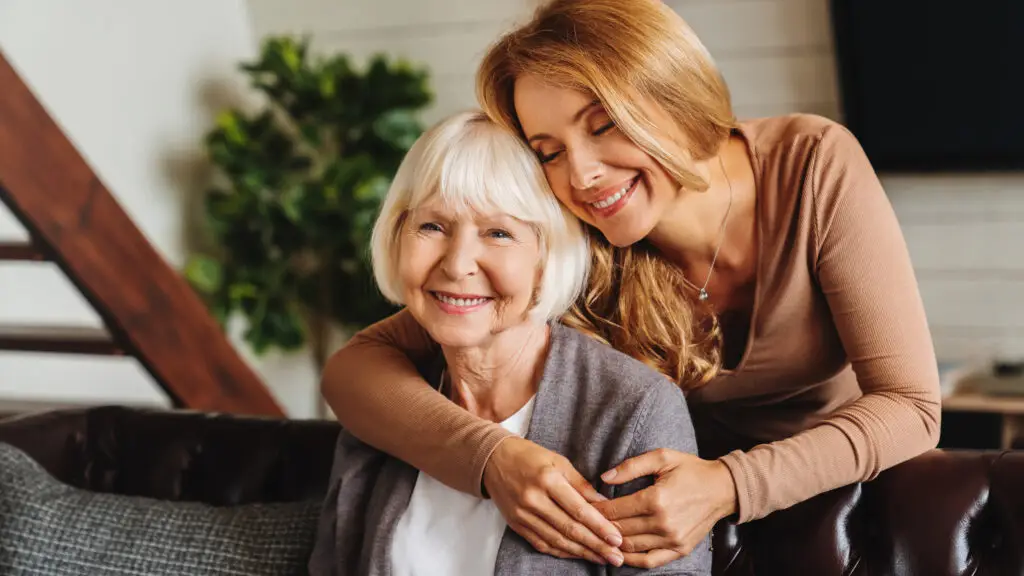 happy daughter embracing from behind elderly mother at living room